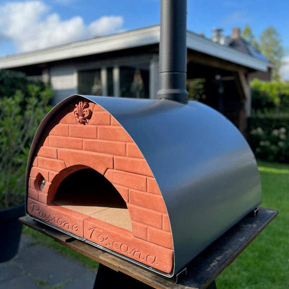 Outdoor brick pizza oven with a metal dome on a stand outdoors.