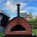 Wood-fired pizza oven with 'Passione Toscana' branding outdoors on a grassy area with houses in the background.